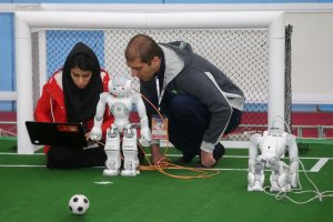 Iranian students programming humanoid robots for a soccer match at a robotics competition, showcasing innovation and STEM education in Iran.